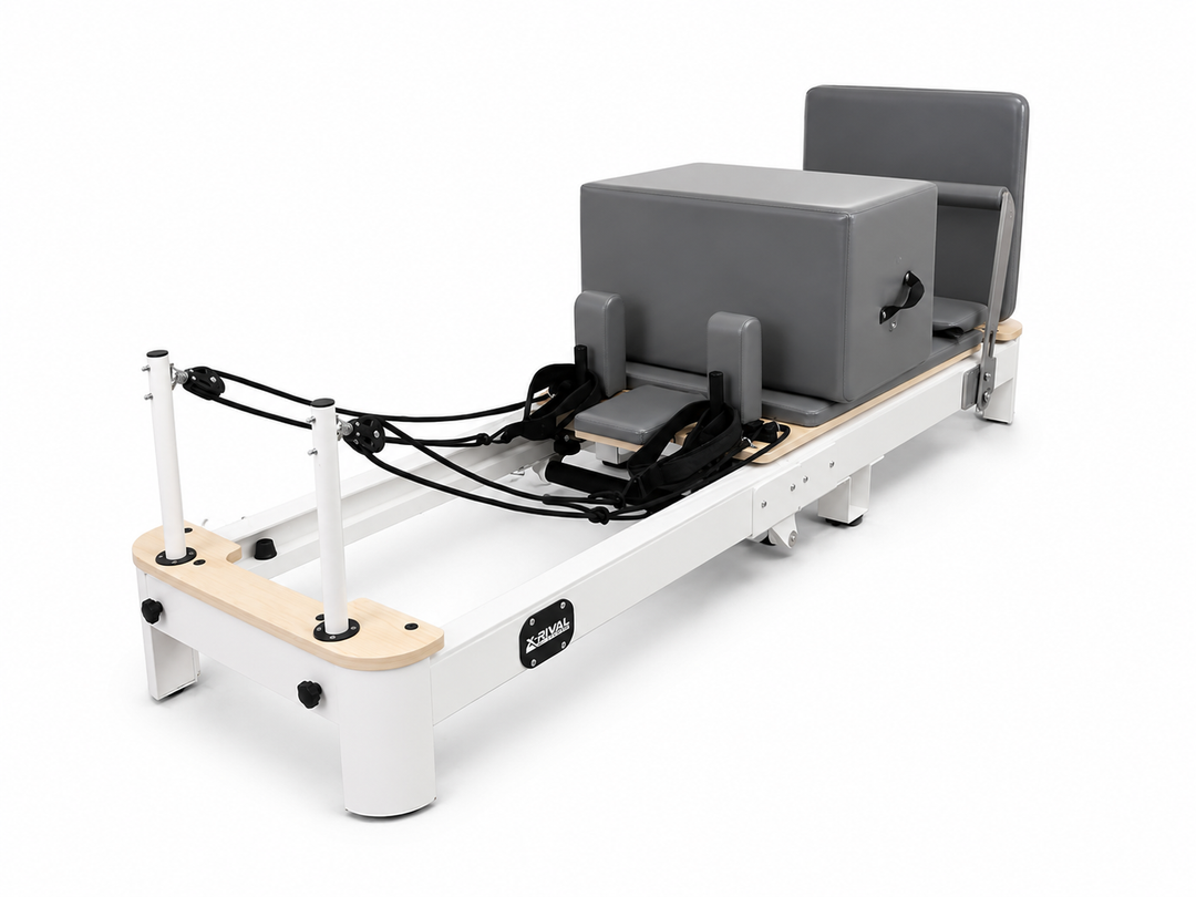 A Pilates reformer machine with a white frame, natural wood accents, black straps, and a gray padded carriage and backrest, shown on a clean white background.