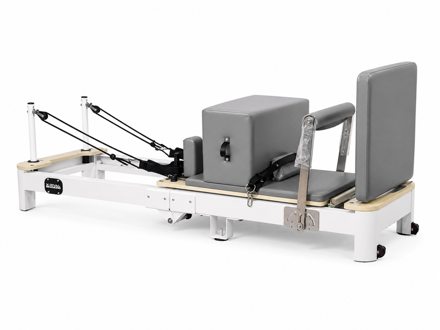 A Pilates reformer machine with gray upholstered padding, a white metal frame, and light wood flooring, shown on a plain white background.