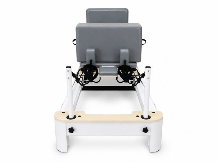 A Pilates reformer machine with a gray padded seat, black handles, and a white frame with a light wood base, shown from the front on a white background.