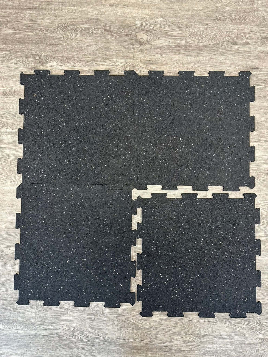 Interlocking rubber mats displayed on a wooden floor, ideal for gym equipment like treadmills and weights.